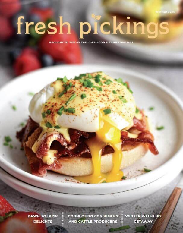 A poached egg on bacon and an English muffin with chives on top, yolk running, on a white plate.