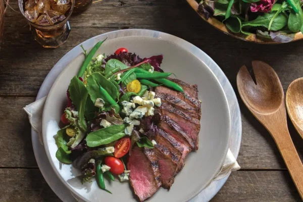 Classic Steakhouse Salad with Blue Cheese, white plate on wooden picnic table, sliced red cherry tomatoes, green lettuce.