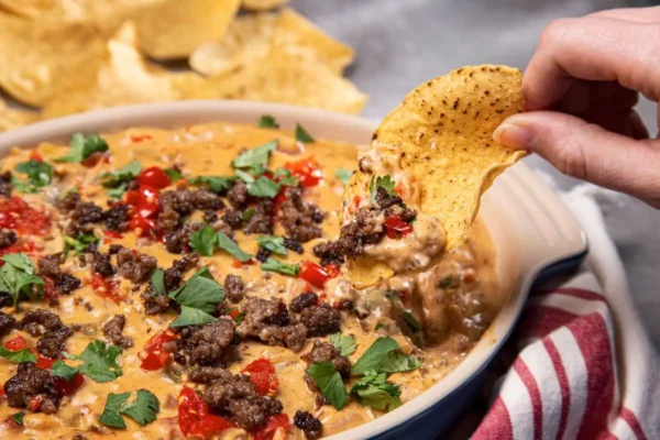 Easy Beef Queso, yellow cheese, ground beef, diced red tomatoes, cilantro and corn ships in white and blue pan.