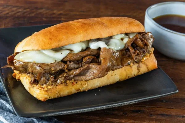 French Dip, hoagie bun with steak slices and white cheese on black tray.