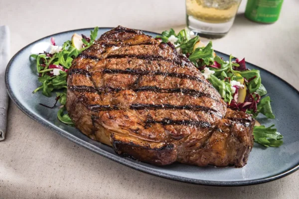 Grilled Ribeye with Arugula, Radicchio and Pear Salad, grey dish and ribeye steak with grill lines on a bed of lettuce.