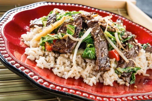 Japanese-Style Sirloin Rice Bowl, red detailed plate with white rice, cooked vegetables, and sirloin steak peices.