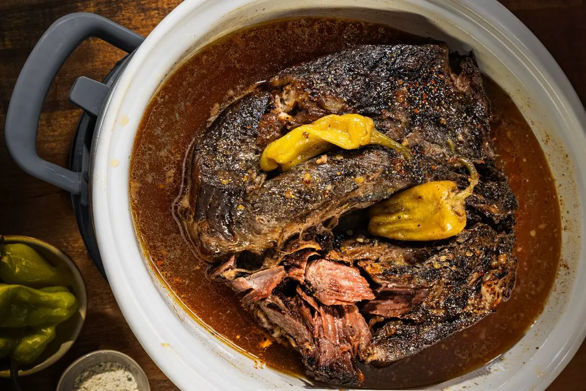 Mississippi Pot Roast, grey slow cooker, white stone dish, yellow peppers, wooden table.