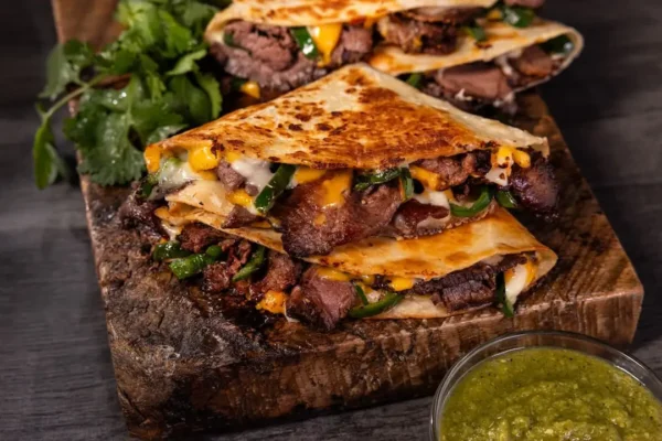 Roast Beef Fajita Quesadilla, fried soft taco shell, greens and cheese on wooden tray.