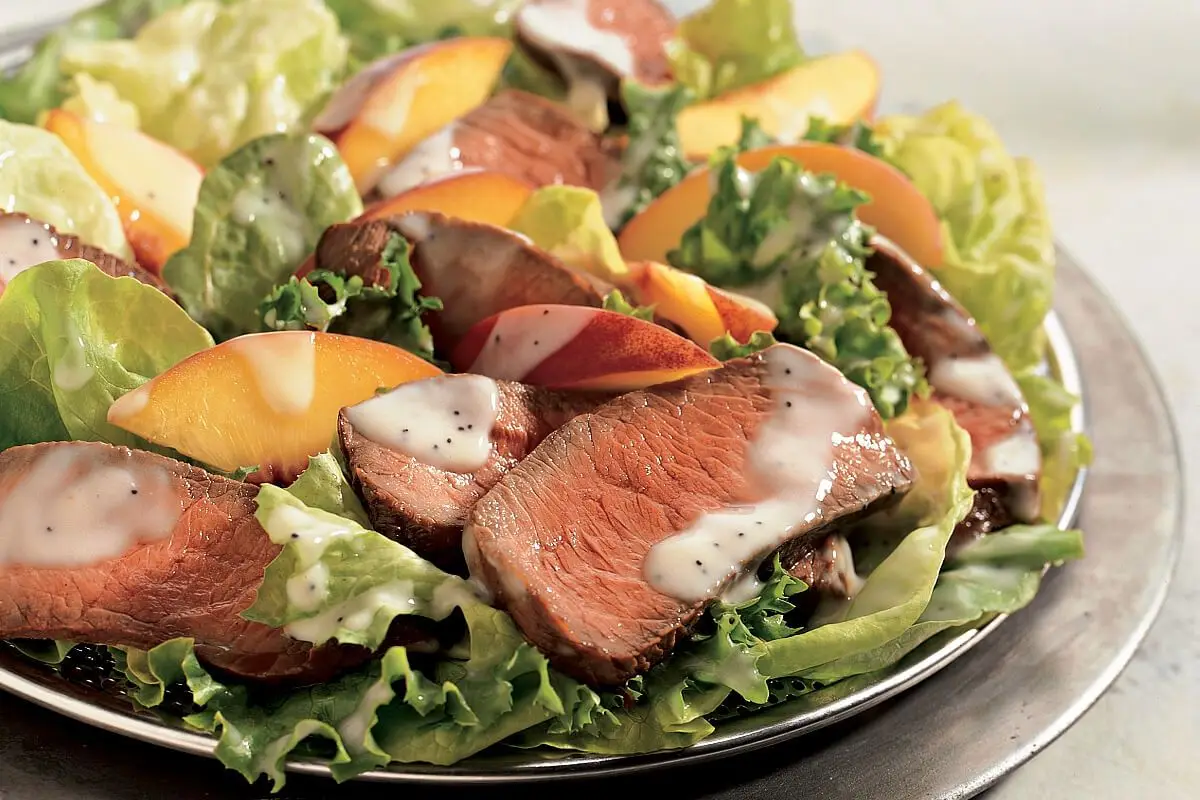 Sirloin Peach Salad, silver plate holding green lettuce, sirloin slices, sliced peaches, and salad dressing.