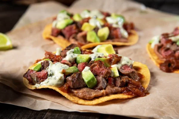 Sirloin Tip Steak Beef Tostadas, diced avocado, parchment paper, green and red and yellow and brown.