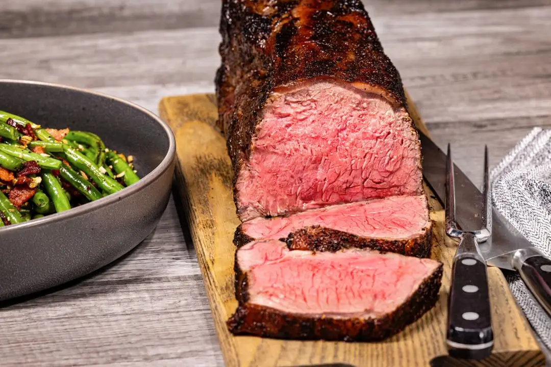 Split Strip Roast with Chef Rub, green beans in grey bowl on the side, served on wooden tray.