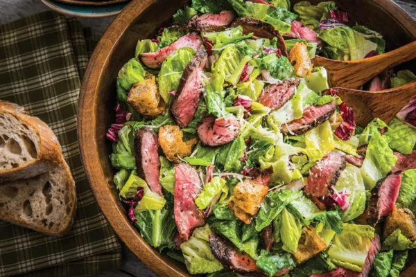 Steak Caesar Salad, iceberg lettuce in wooden bowl with parmesan and steak, wooden utensils.