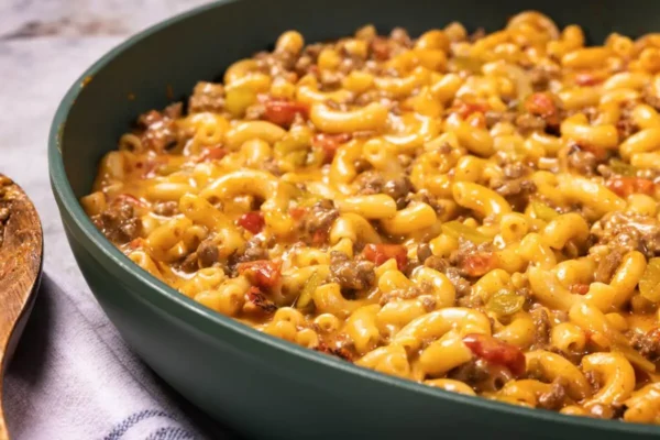 Taco Macaroni and Cheese, yellow mac and cheese, red tomato peices, ground beef, green pan on a plaid towel.