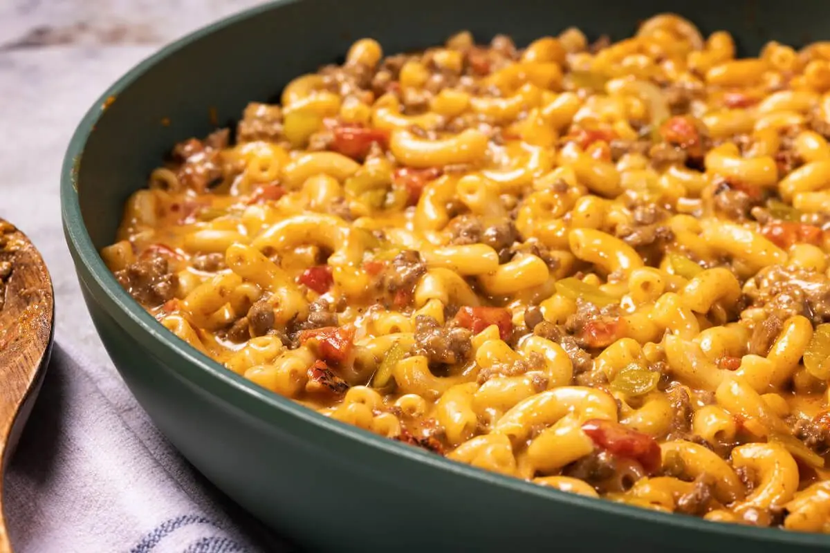 Taco Macaroni and Cheese, yellow mac and cheese, red tomato peices, ground beef, green pan on a plaid towel.